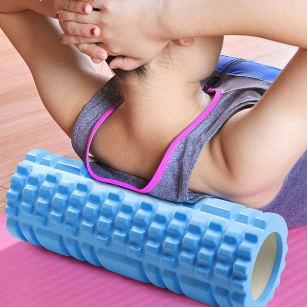 Woman using a blue yoga roller for back muscle relaxation on a mat.