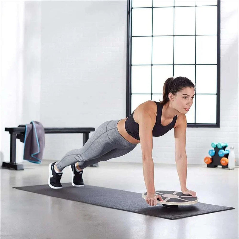 Woman performing a plank using a wooden balance board on a yoga mat in a home gym setting.